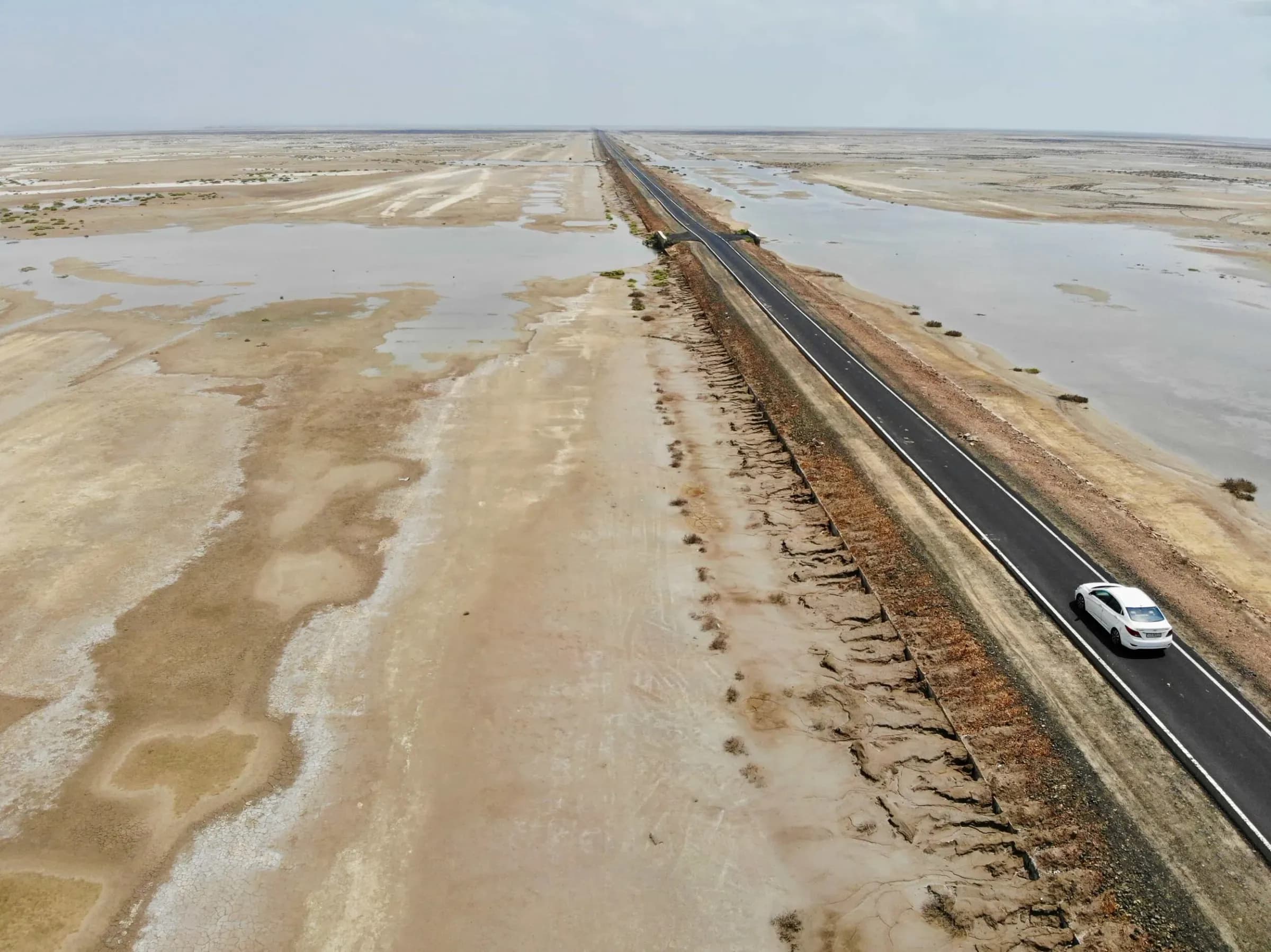 Aerial drone shot of a single car driving down a long road across the Odisha salt flats