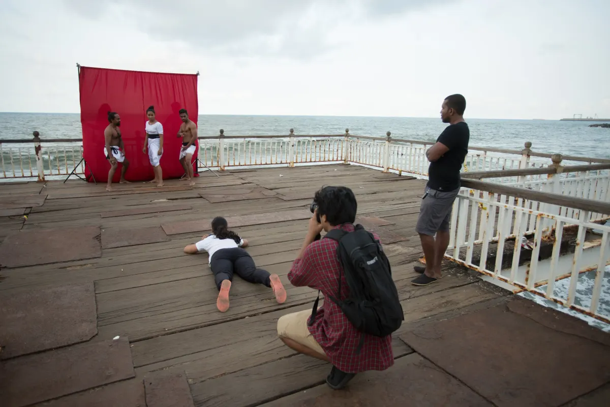 Angampora martial artists posing for a photoshoot against a red backdrop by the sea, Colombo