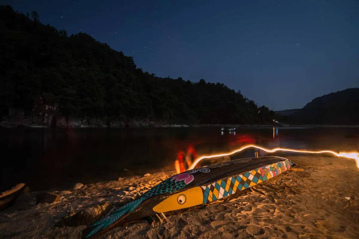 A hand-painted fishing boat glowing by firelight on the banks of the Dawki river at night