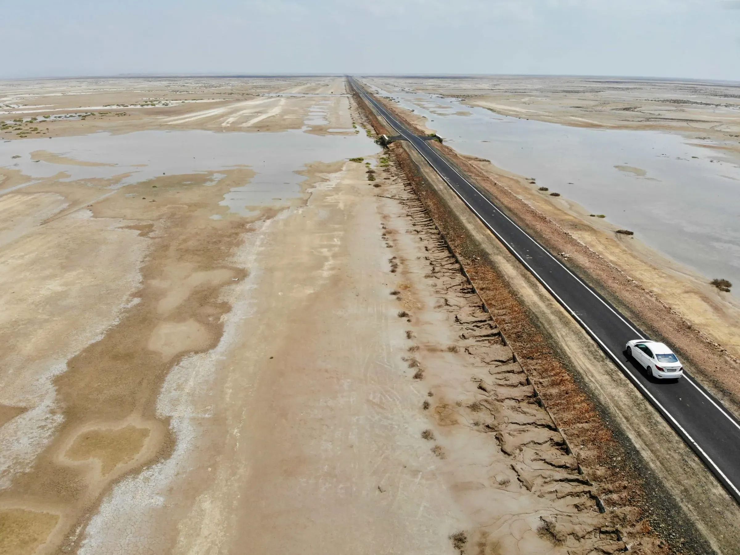 Aerial view of a coastal salt-flat road in Odisha with a single car driving through