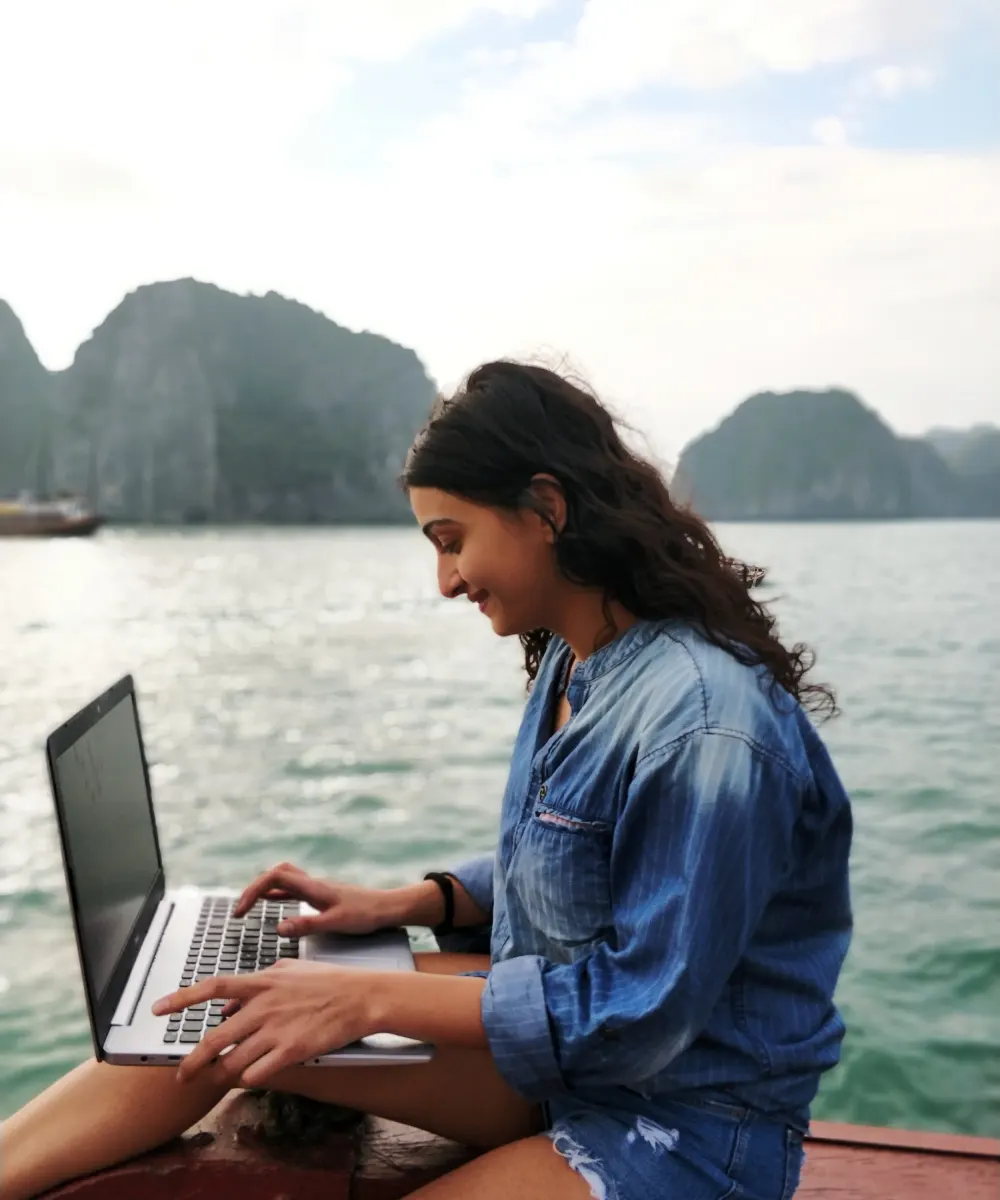A creator working on a boat with the limestone cliffs of Ha Long Bay behind her